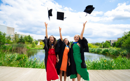 Three UCD alumnae throwing their graduation caps in the air.